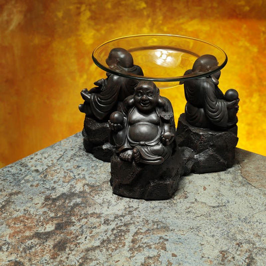 Decorative oil burner with Buddha statues on a stone surface against an orange background